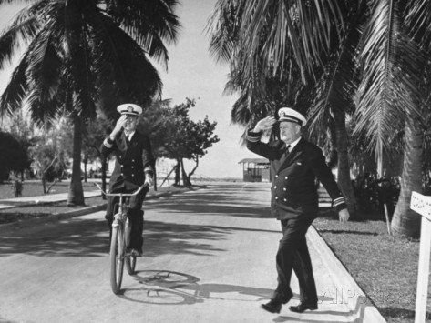 A lieutenant commander riding a bicycle saluting a lieutenant commander crossing the street